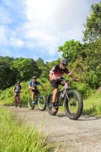 Three cyclists enjoy mountain biking through lush greenery in Batangas, Philippines.