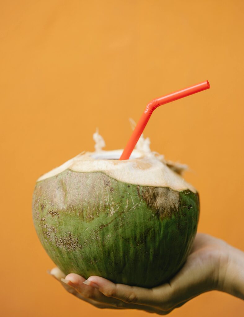 pexels-photo-5945745-5945745 A hand holds a fresh coconut drink with a red straw against an orange background, exuding tropical vibes.